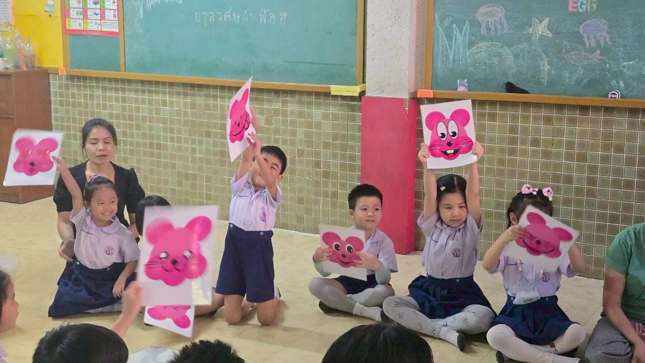 Children holding up pink mouse drawings in a classroom